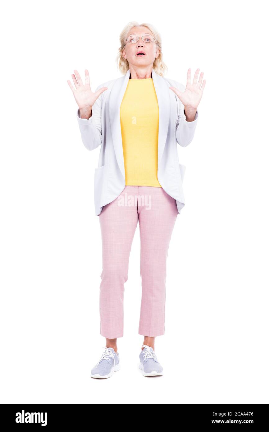 Vertical full shot of aged woman wearing casual clothes standing against white background feeling astonished and scared Stock Photo