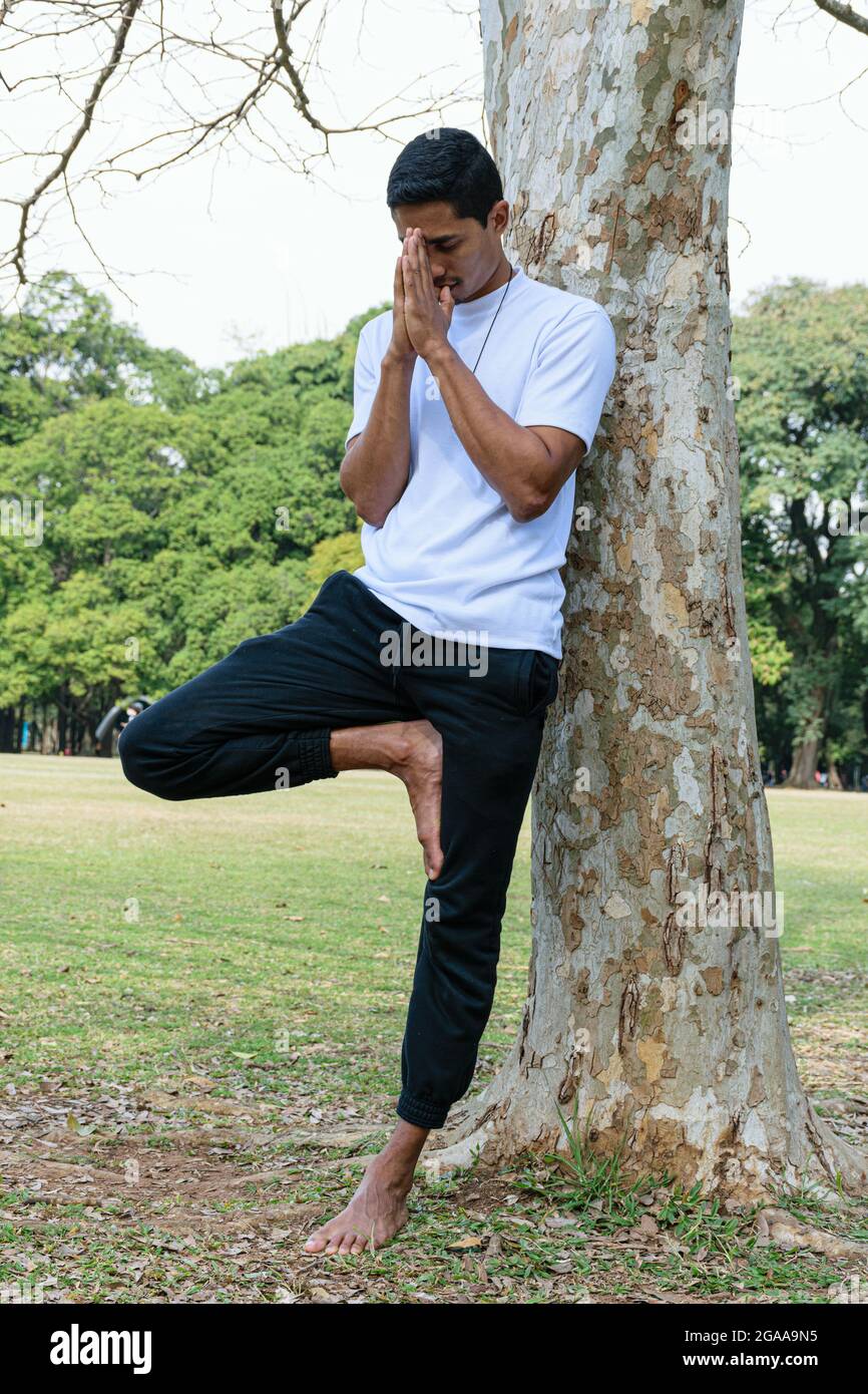 Brazilian young man leaning against a tree, with his hands close to his face, in a salute position. Stock Photo