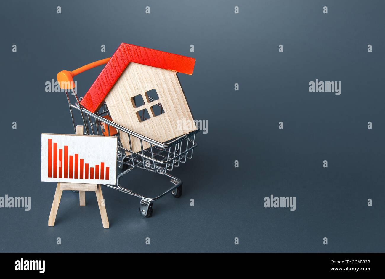 House in a cart and an red decline graph on easel. Low property value, low price. Fall of the market. Lower mortgage interest rates. Falling prices fo Stock Photo