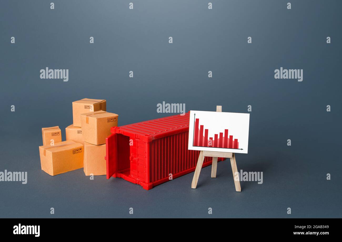 Boxes and container near the easel with falling graph. Drop of transportation volume, world trade traffic reduction. Fall in sales. Reduced prices for Stock Photo