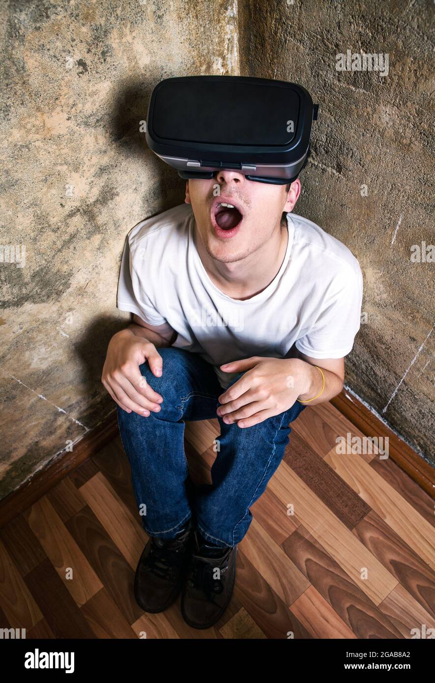 Surprised Young Man in Virtual Reality Glasses sit on the Floor by the Old Wall Stock Photo