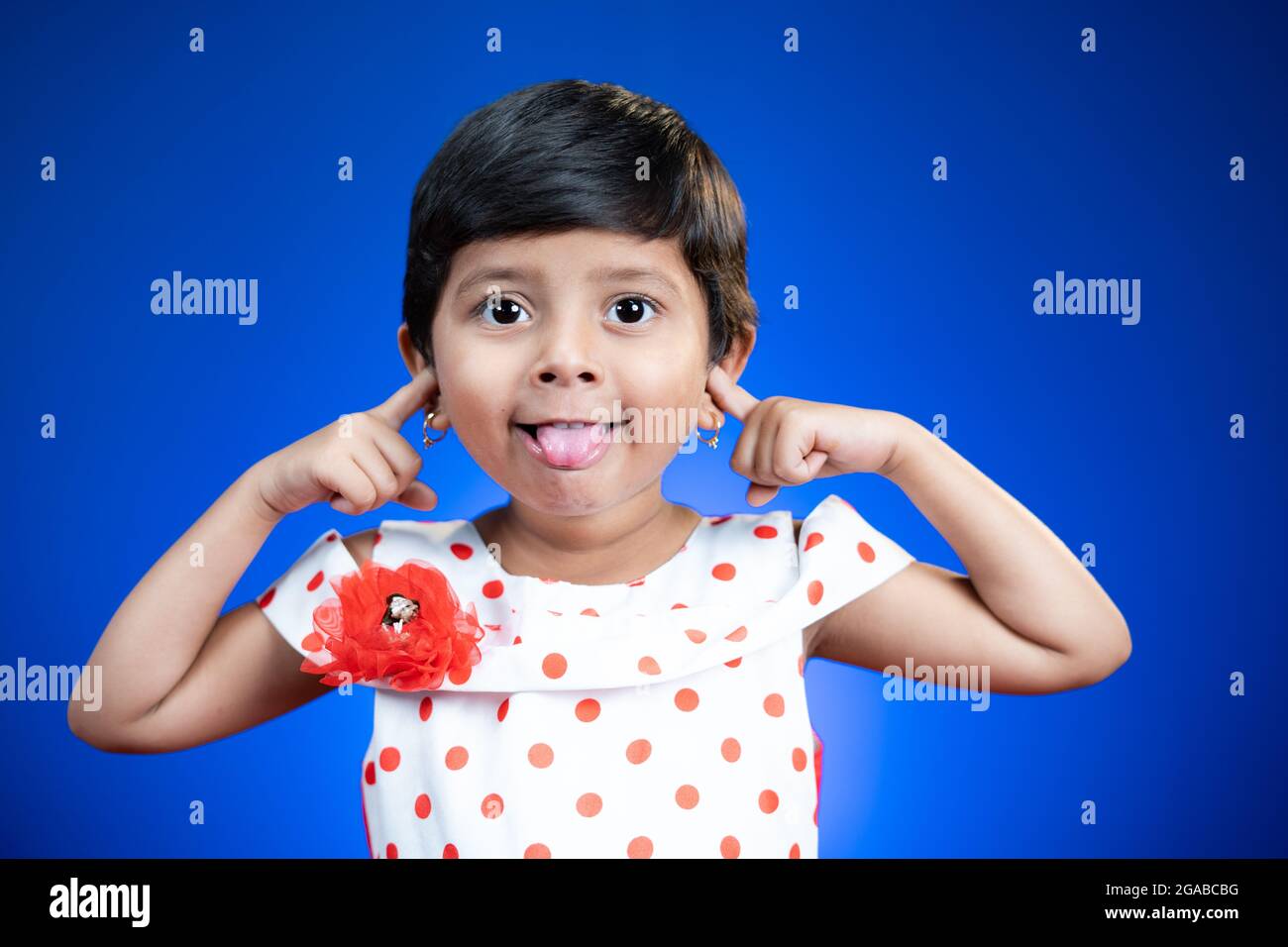 Litte girl kid with tongue out or grimacing dancing on blue background - happy, cheerful and crazy kids concept. Stock Photo