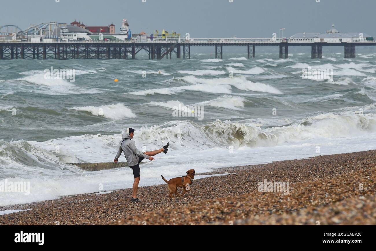 Brighton UK 30th July 2021 - A runner kicks a ball for his dog on Brighton beach early this morning as Storm Evert sweeps across the country with wind speeds forecast to be up to 60mph in some areas : Credit Simon Dack / Alamy Live News Stock Photo