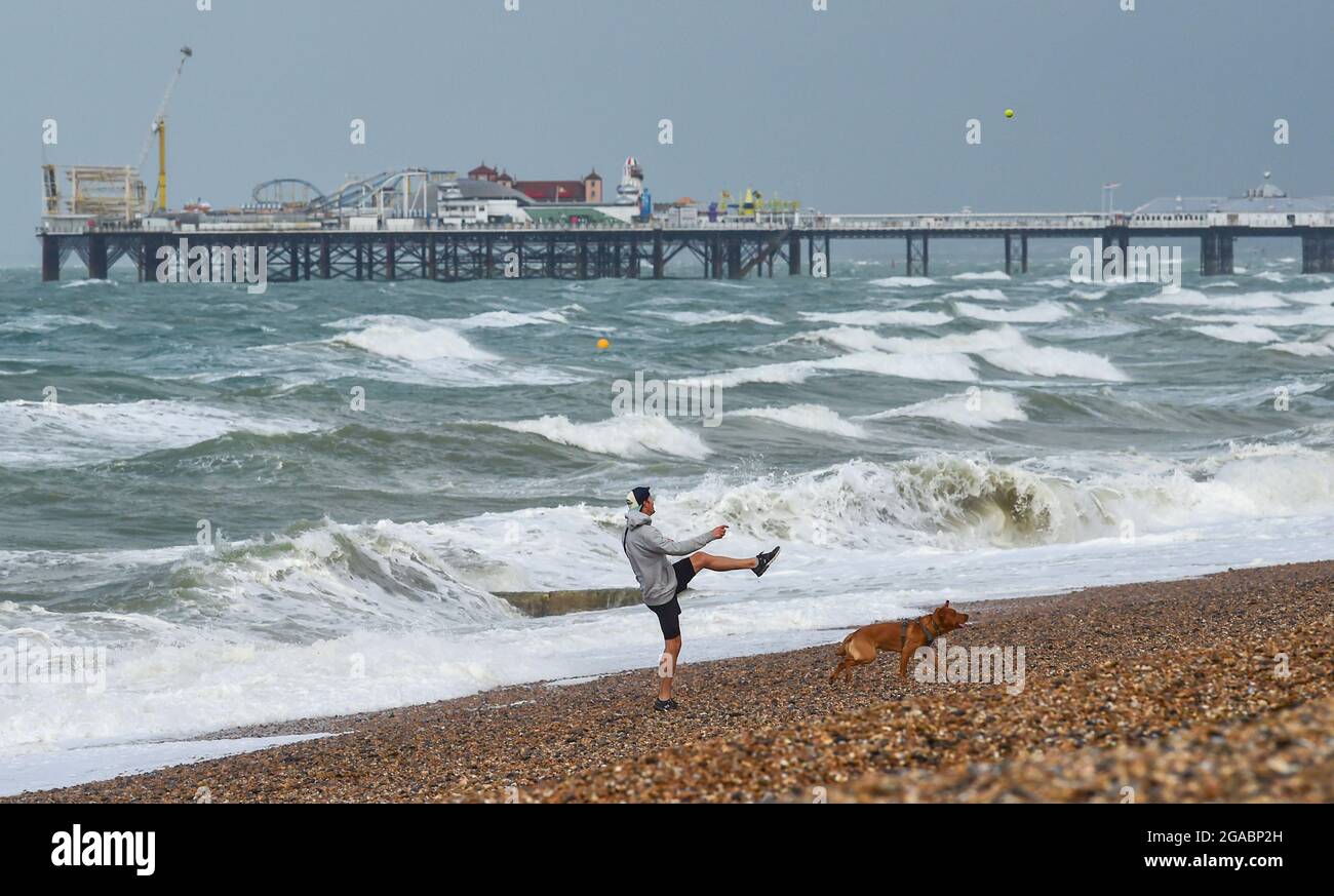 Brighton UK 30th July 2021 - A runner kicks a ball for his dog on Brighton beach early this morning as Storm Evert sweeps across the country with wind speeds forecast to be up to 60mph in some areas : Credit Simon Dack / Alamy Live News Stock Photo