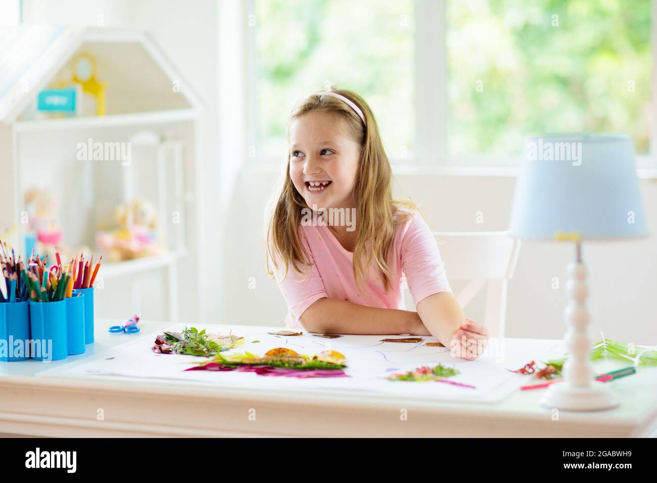 Child creating picture with colorful leaves. Art and crafts for kids. Little girl making collage image with rainbow plant leaf. Biology homework Stock Photo