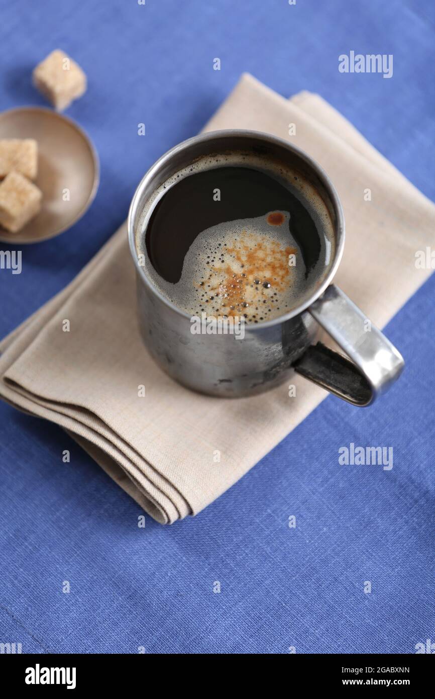 Metal cup of flavored coffee with lump sugar and flowers on table with ...