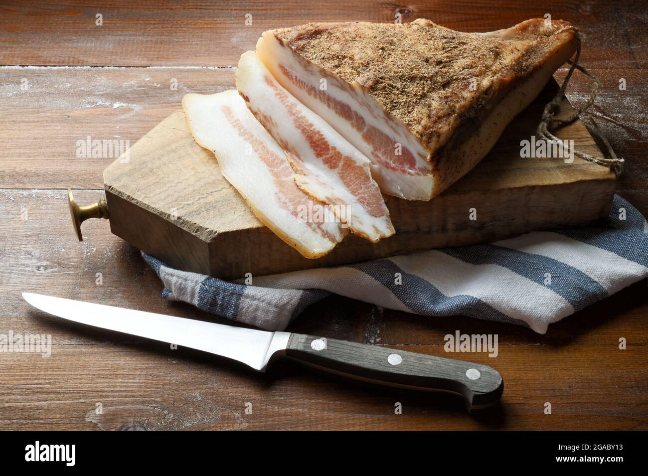 Guanciale Amatriciano with cutting board and knife on wooden table. The guanciale is a pork sausage typical of central Italy. Close-up, space for text Stock Photo