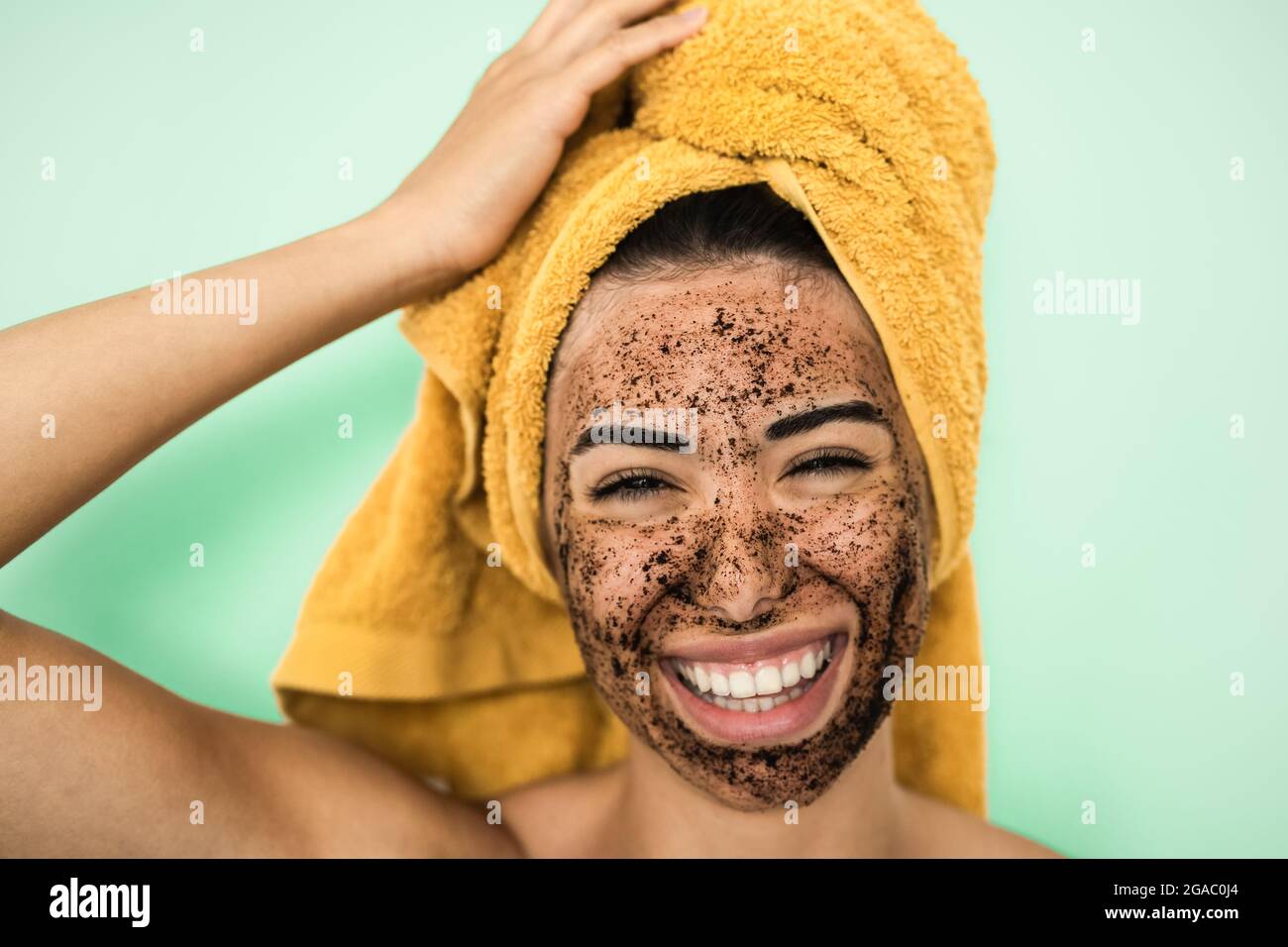 Young smiling woman applying coffee scrub mask on face - Happy girl having skin care spa day at home Stock Photo