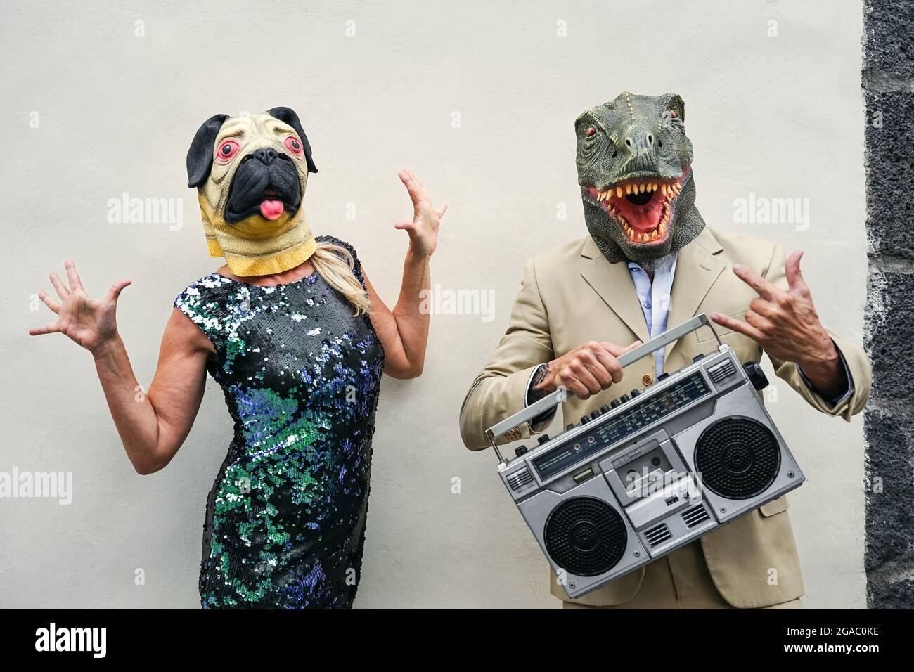 Happy senior couple having fun wearing dog and t-rex mask - Mature people celebrating carnival holidays while dancing and listening music Stock Photo