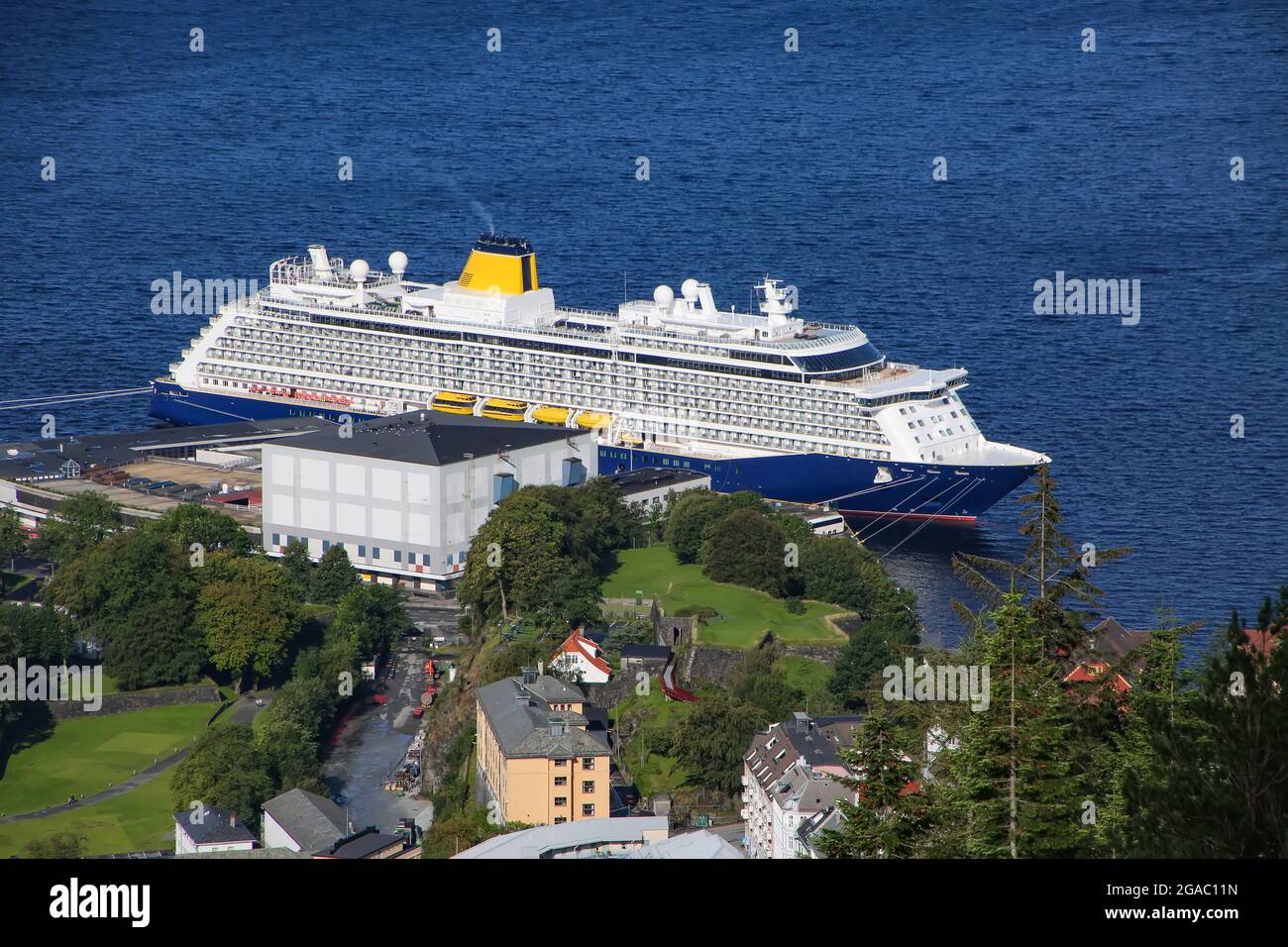 View of a cruise ship with dark blue hull & yellow funnel, docked in the port from the top of the Floibanen funicular and Mount Fløyen, Bergen, Norway. Stock Photo