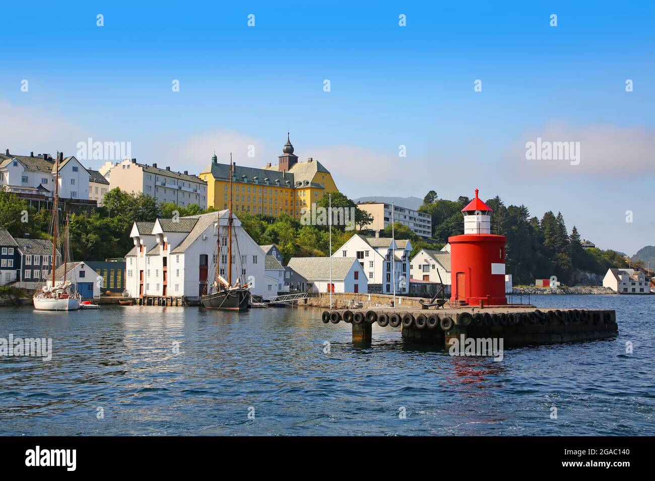 Historic buildings, pier and traditional fishing boats along the waterfront of the harbour. Lighthouse in the foreground of the getty, Alesund, Norway Stock Photo