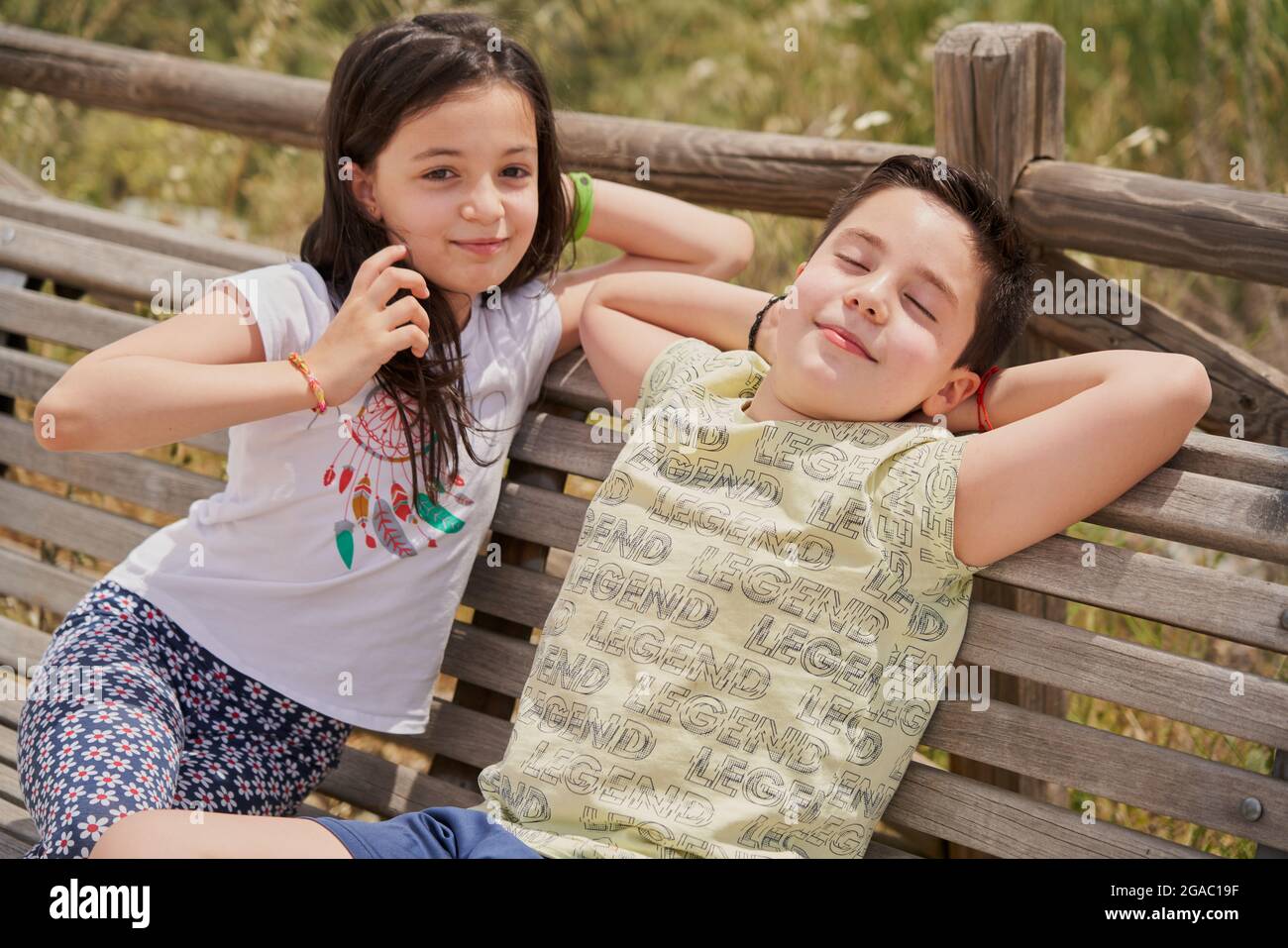 MOSTOLES, SPAIN - May 22, 2021: Children sitting on wooden bench laughing relaxed in park Stock Photo