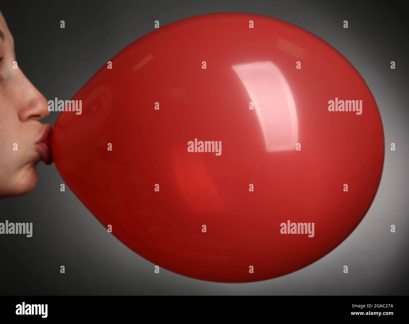 Young woman inflating balloon on gray background Stock Photo - Alamy