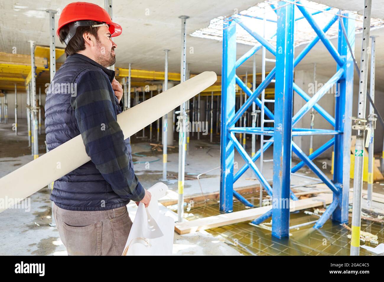 Architect with hard hat and building drawing in the shell of the construction site of the house building Stock Photo