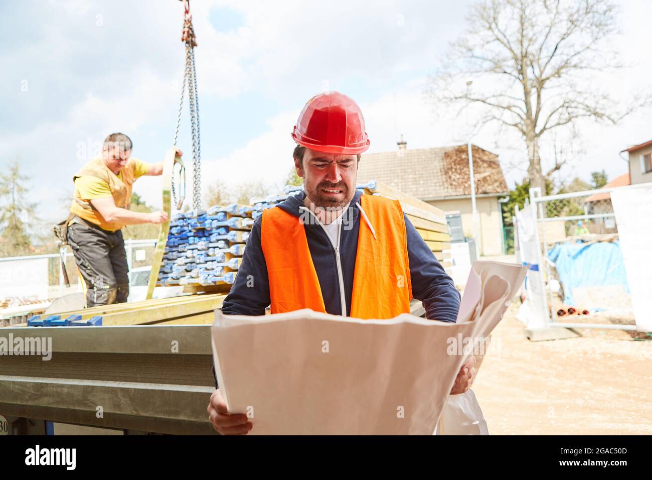 Foreman at the construction site with construction drawing and with construction material delivery in the background Stock Photo