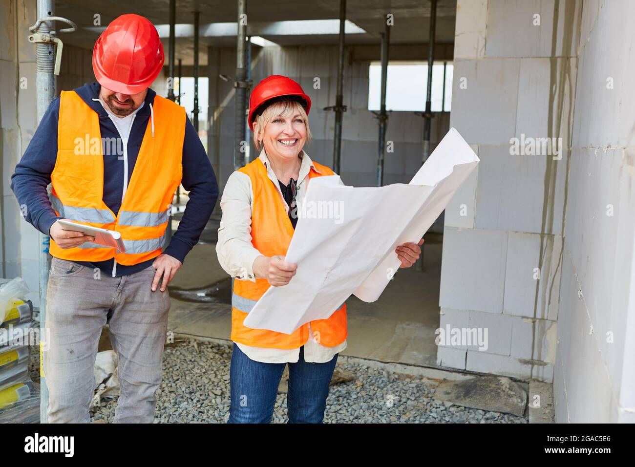 Craftsman and smiling architect with building drawing together in front of a shell as a new building Stock Photo