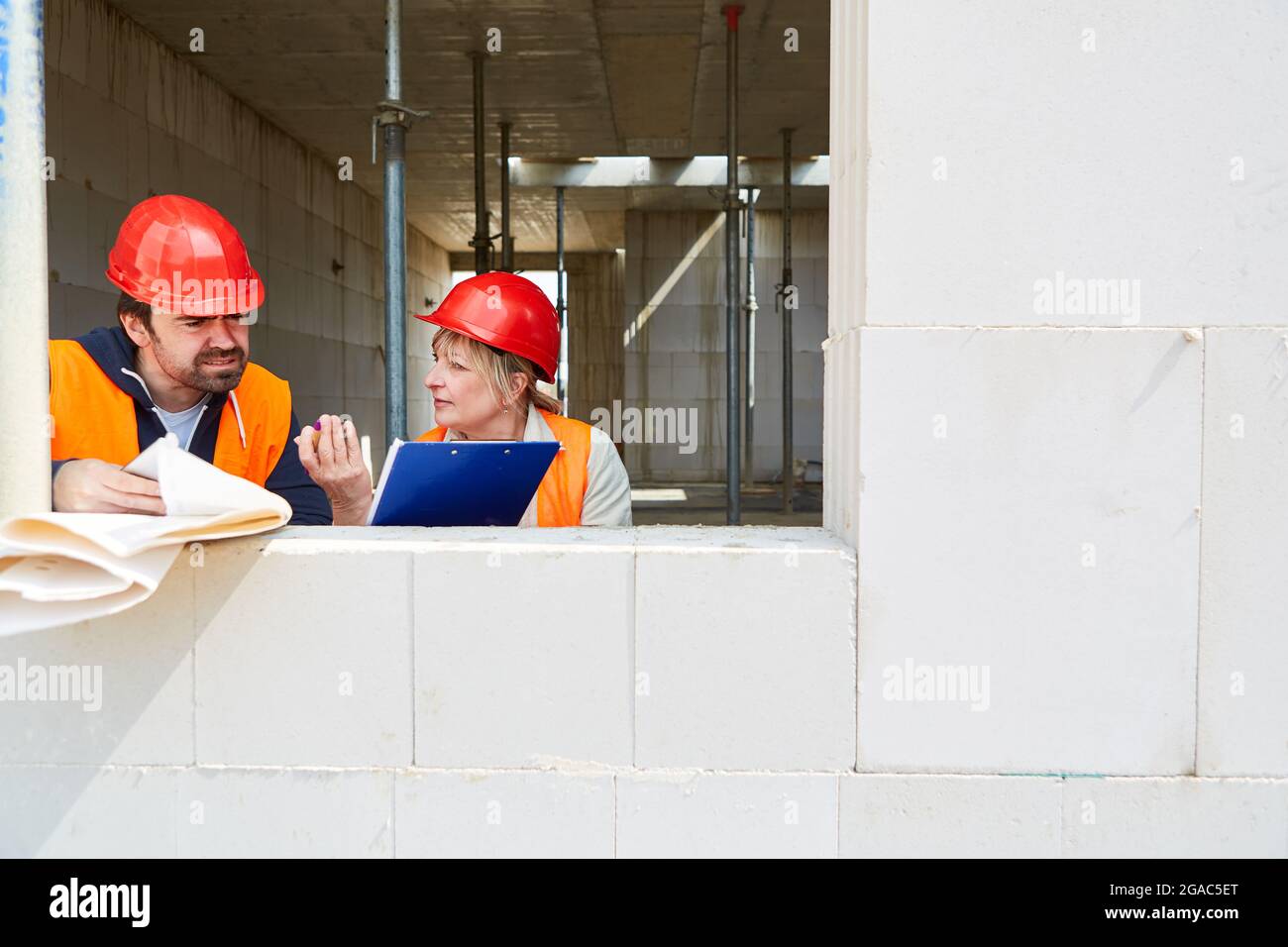 Architect with checklist and foreman discussing the construction project in the shell of the construction site Stock Photo