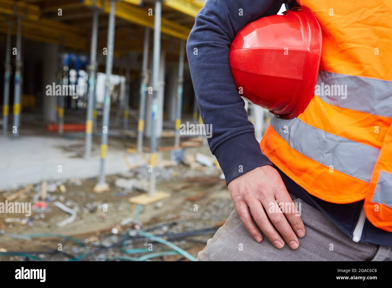 Construction worker with red hard hat and safety vest in orange on a building site under construction Stock Photo