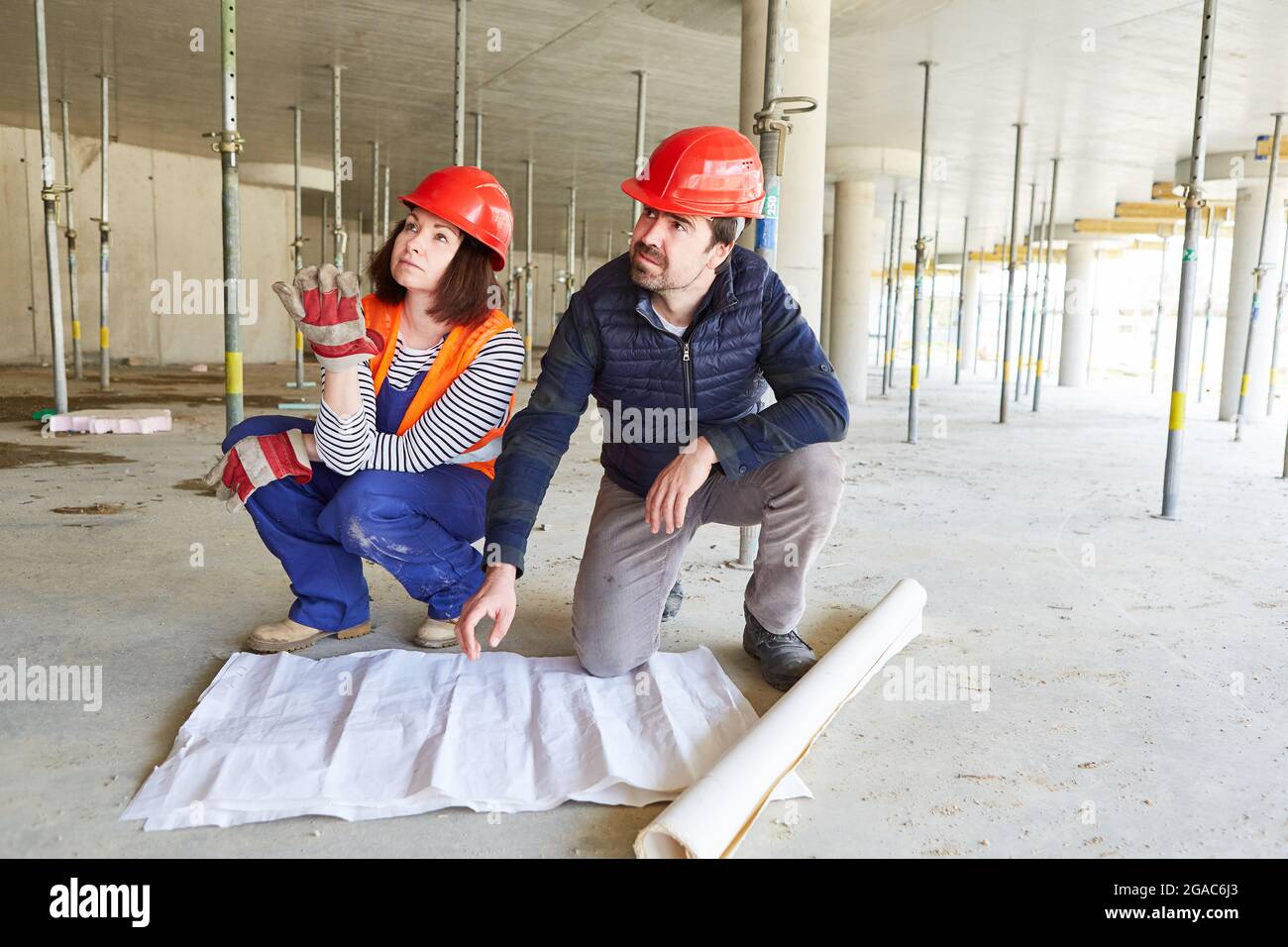 Architect and worker with architectural drawing when planning the construction project in the shell of the construction site Stock Photo