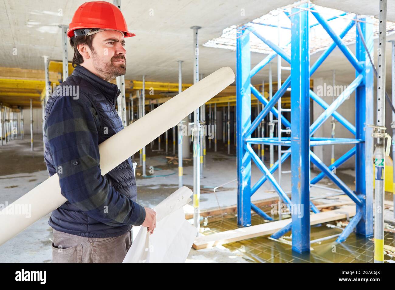 Thoughtful architect or foreman with blueprint in the shell of the construction site of building a house Stock Photo