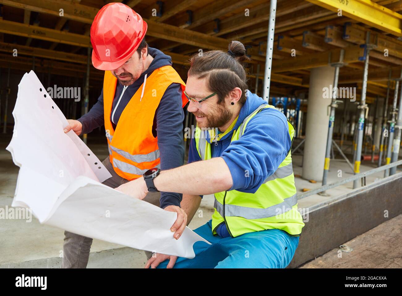Craftsmen and construction workers with building drawings together in front of a new building as a shell Stock Photo