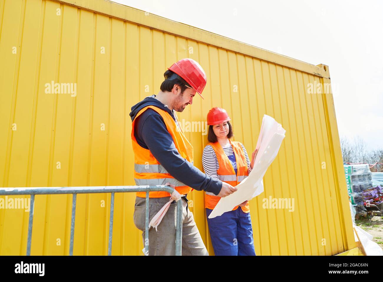 Craftsman and architect with blueprint in front of a yellow container during a construction project meeting Stock Photo