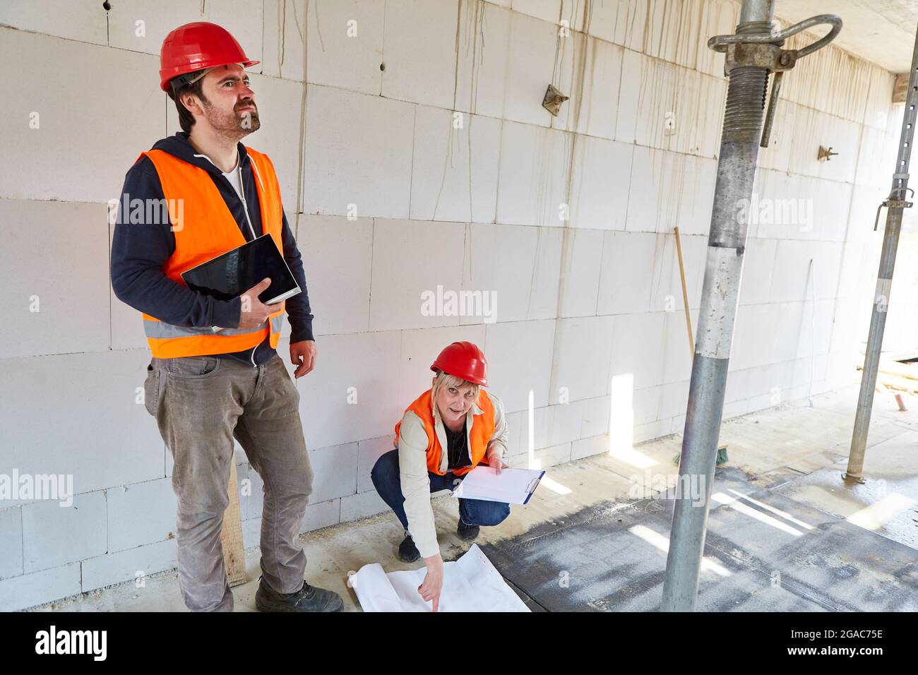 An architect with a blueprint and a building expert in the shell construction inspect the construction site of the house Stock Photo