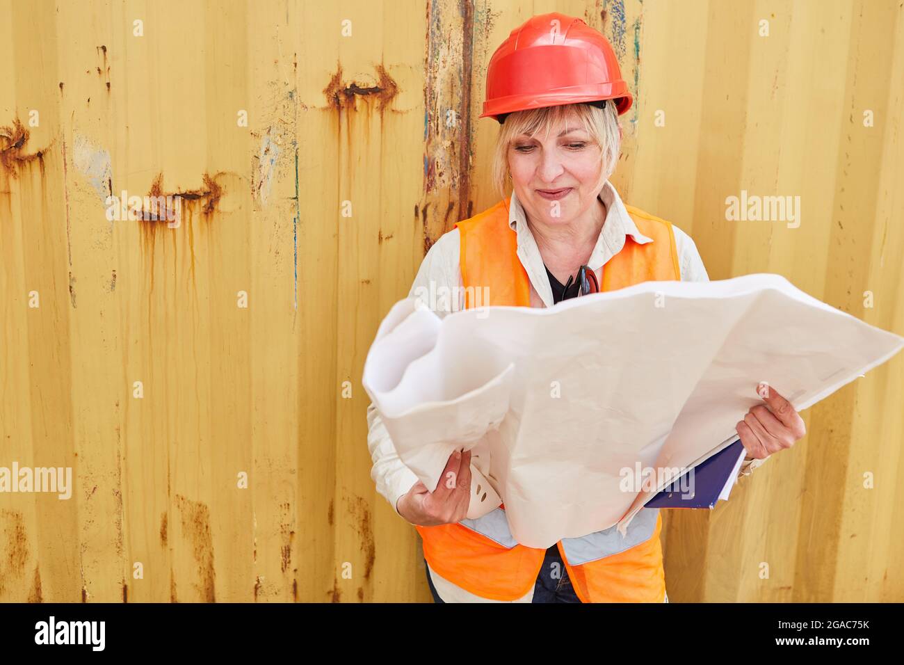 Woman as a construction worker or architect with a red hard hat looks at construction drawing for house construction Stock Photo