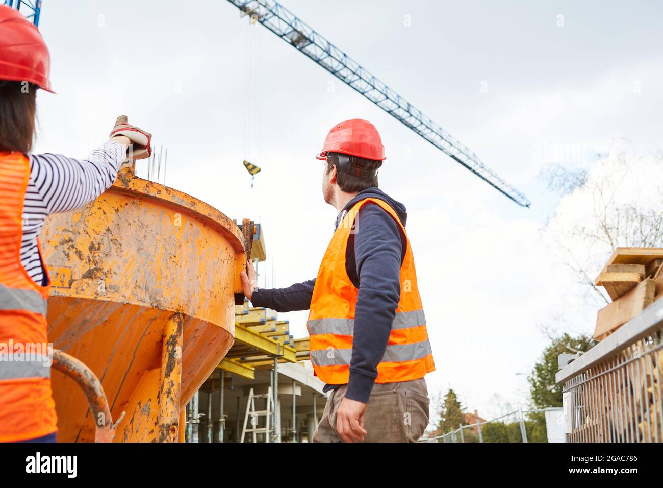 Workers team on the construction site of the new building at the cement mixer with construction crane in the background Stock Photo