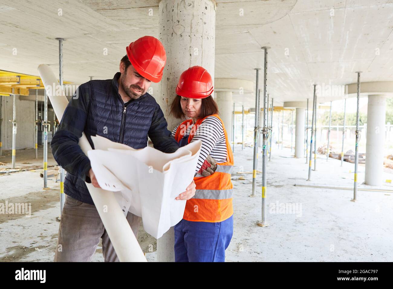 Architect with construction drawing and workers together in the construction planning in the shell of the construction site Stock Photo