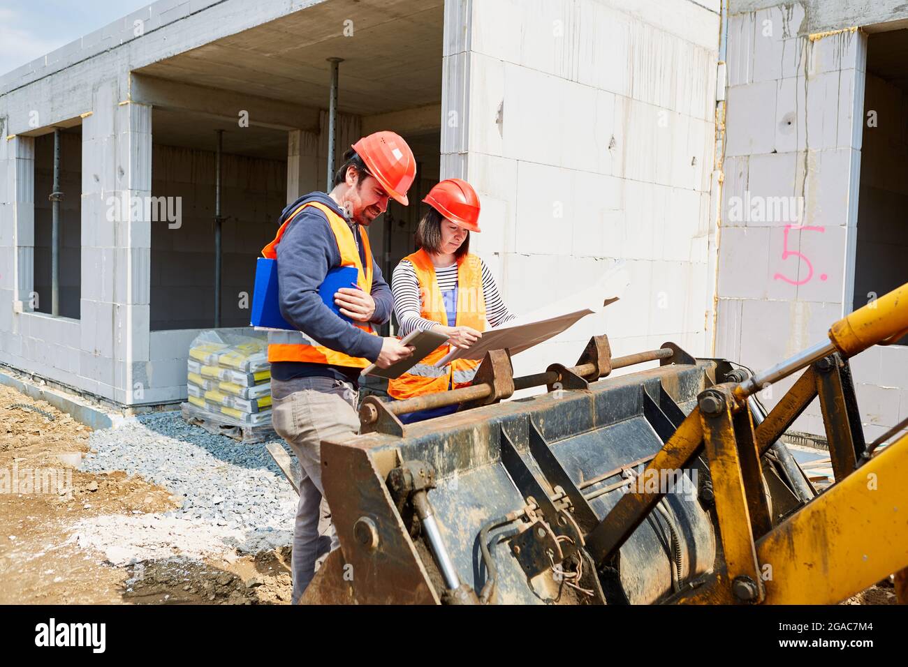 Architect and craftsman in front of an excavator look at the construction plan on a building site in the shell Stock Photo