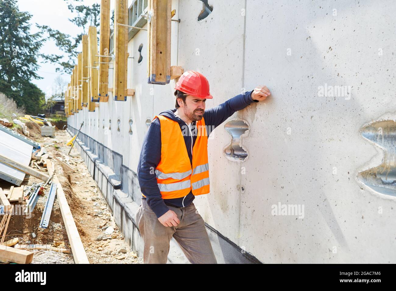 Construction worker as a foreman with a red hard hat is standing on the facade of a building site under construction Stock Photo