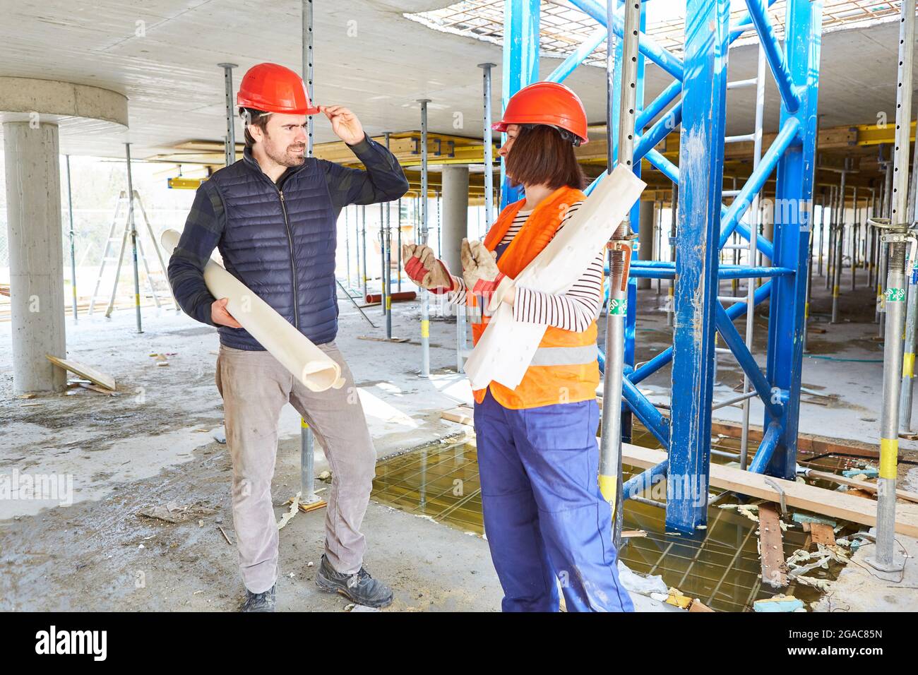 Architect with architectural drawing and craftsman discuss building project on the building site in the shell Stock Photo