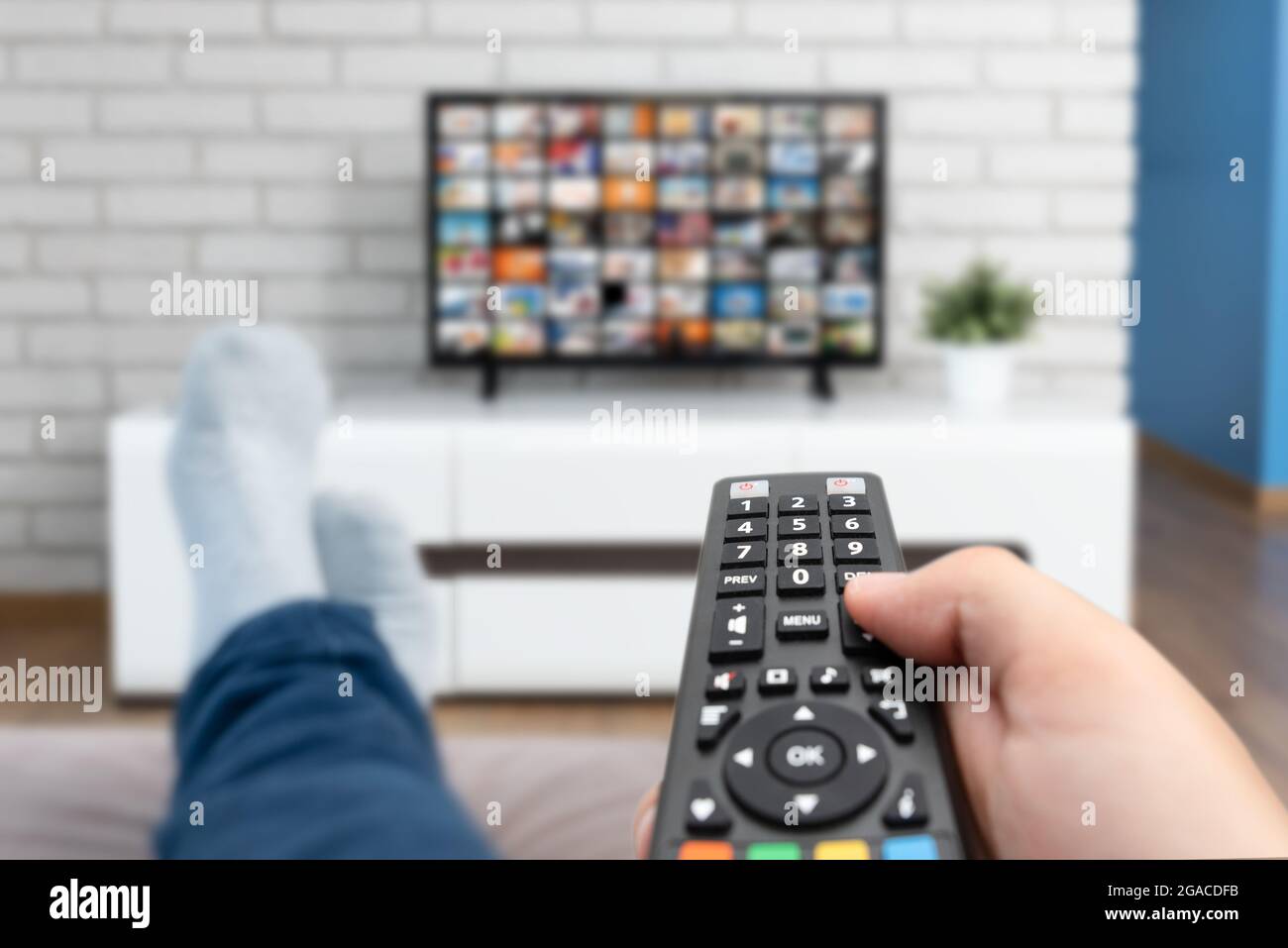 Man watching TV, lying on sofa, legs on table. Person holding remote control in living room Stock Photo