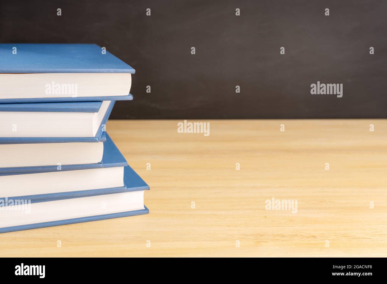 Pile of books on wooden table and black chalkboard at background with copy space. Back to school, education or learning concept Stock Photo