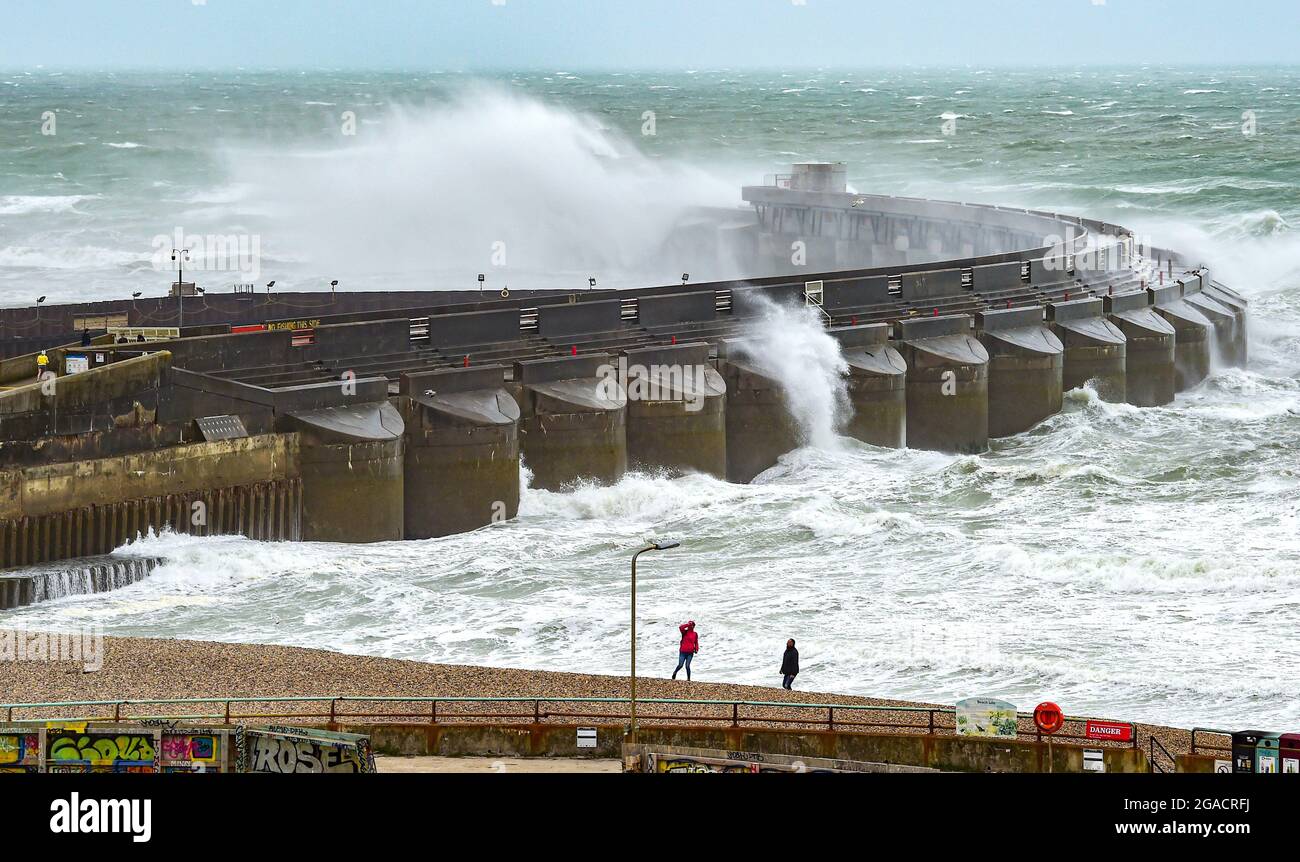Brighton UK 30th July 2021 - Walkers on the beach by  Brighton Marina west wall as Storm Evert sweeps across the country with wind speeds forecast to be up to 60mph in some areas : Credit Simon Dack / Alamy Live News Stock Photo