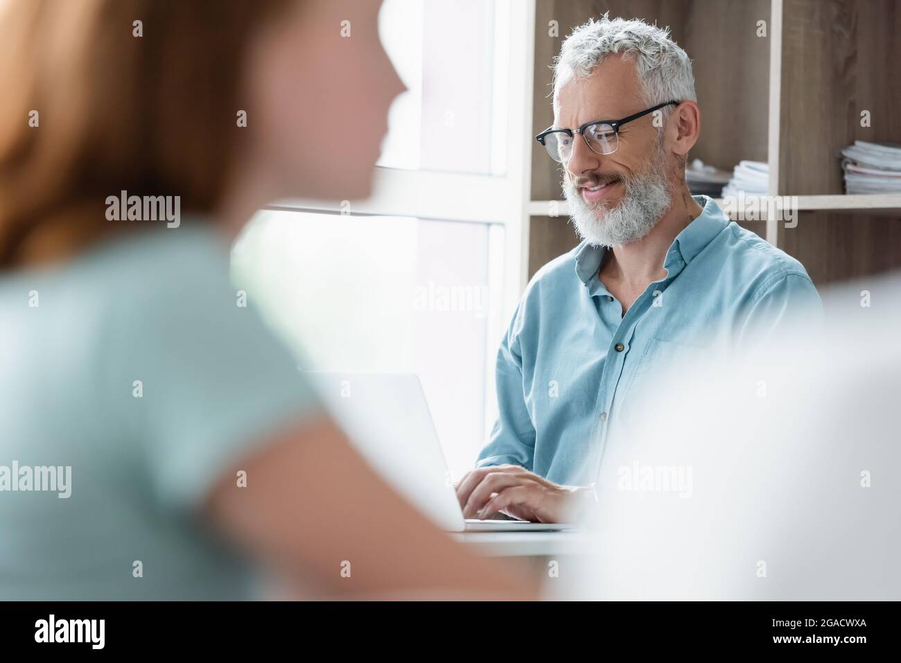Happy teacher using laptop near blurred child in classroom Stock Photo ...