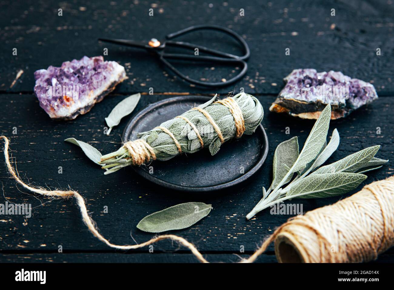 White homemade sage Salvia apiana smudge stick at home with homegrown sage leaves. Cotton string, vintage scissors and amethyst clusters. Stock Photo