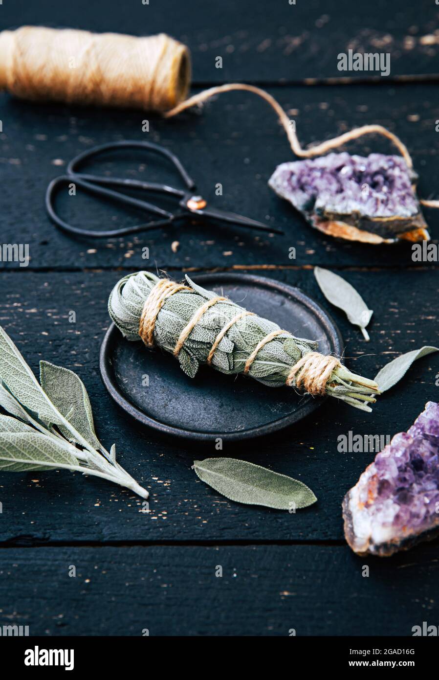White homemade sage Salvia apiana smudge stick at home with homegrown sage leaves. Cotton string, vintage scissors and amethyst clusters. Stock Photo