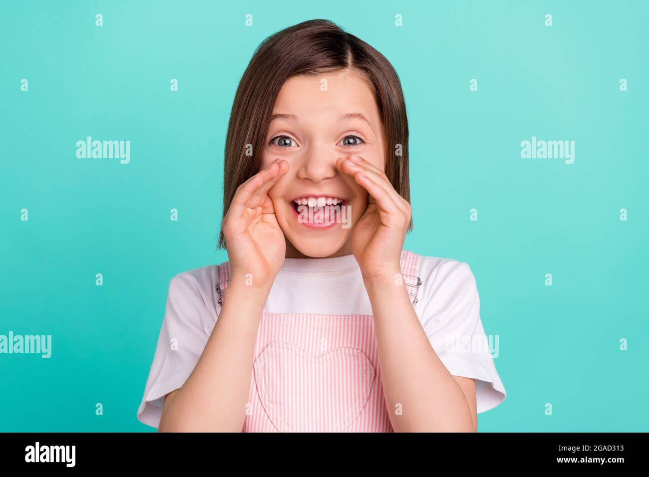 Photo of cheerful amazed happy little girl hold hands mouth face tell news isolated on teal color background Stock Photo