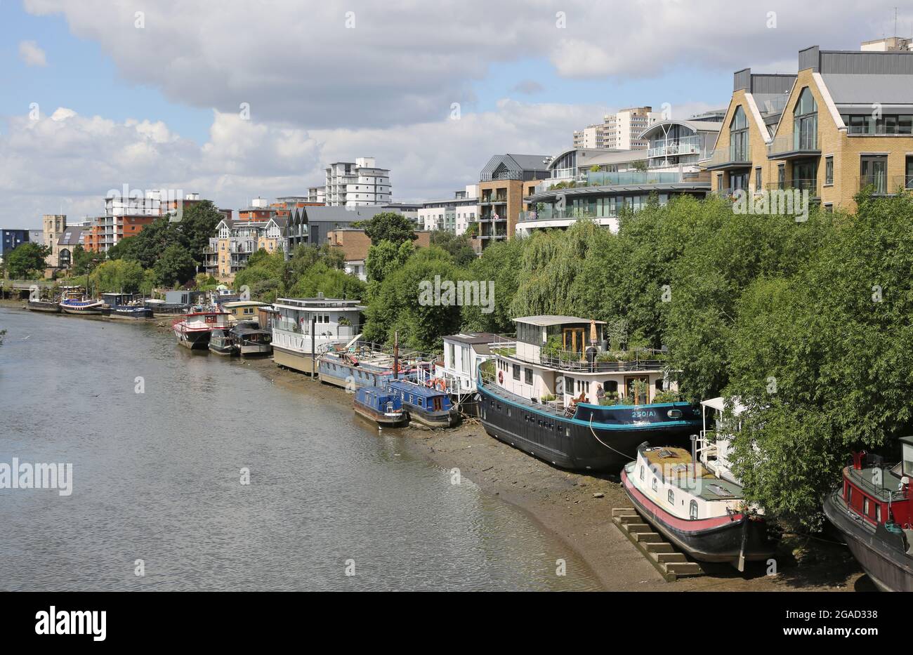 House boats moored on the north bank of the River Thames west of Kew Bridge, London, UK. Hulls rest on timver beams to keep them level at low tide. Stock Photo