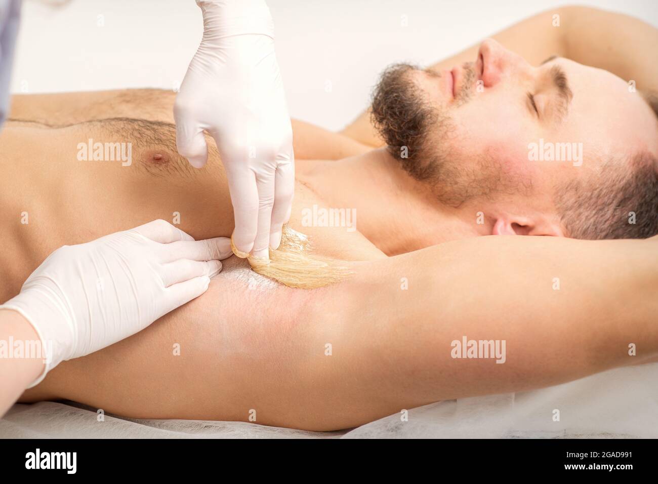 Young caucasian man receiving hair removal from his armpit in a beauty salon, depilation men's underarm Stock Photo