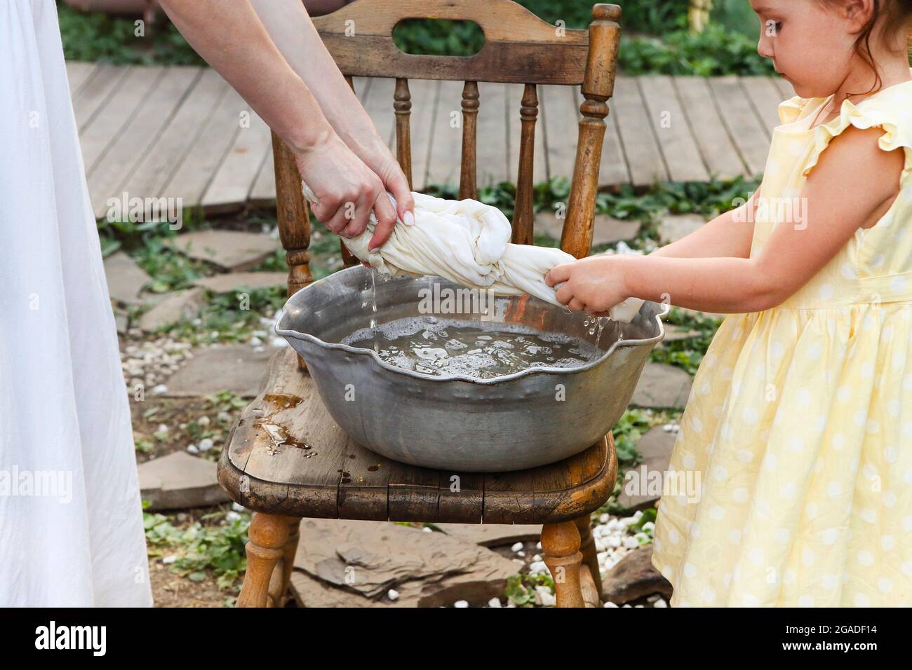 Mom and little daughter spending time and doing household chores together outside in village, closeup of woman and cute girl standing and twisting lin Stock Photo