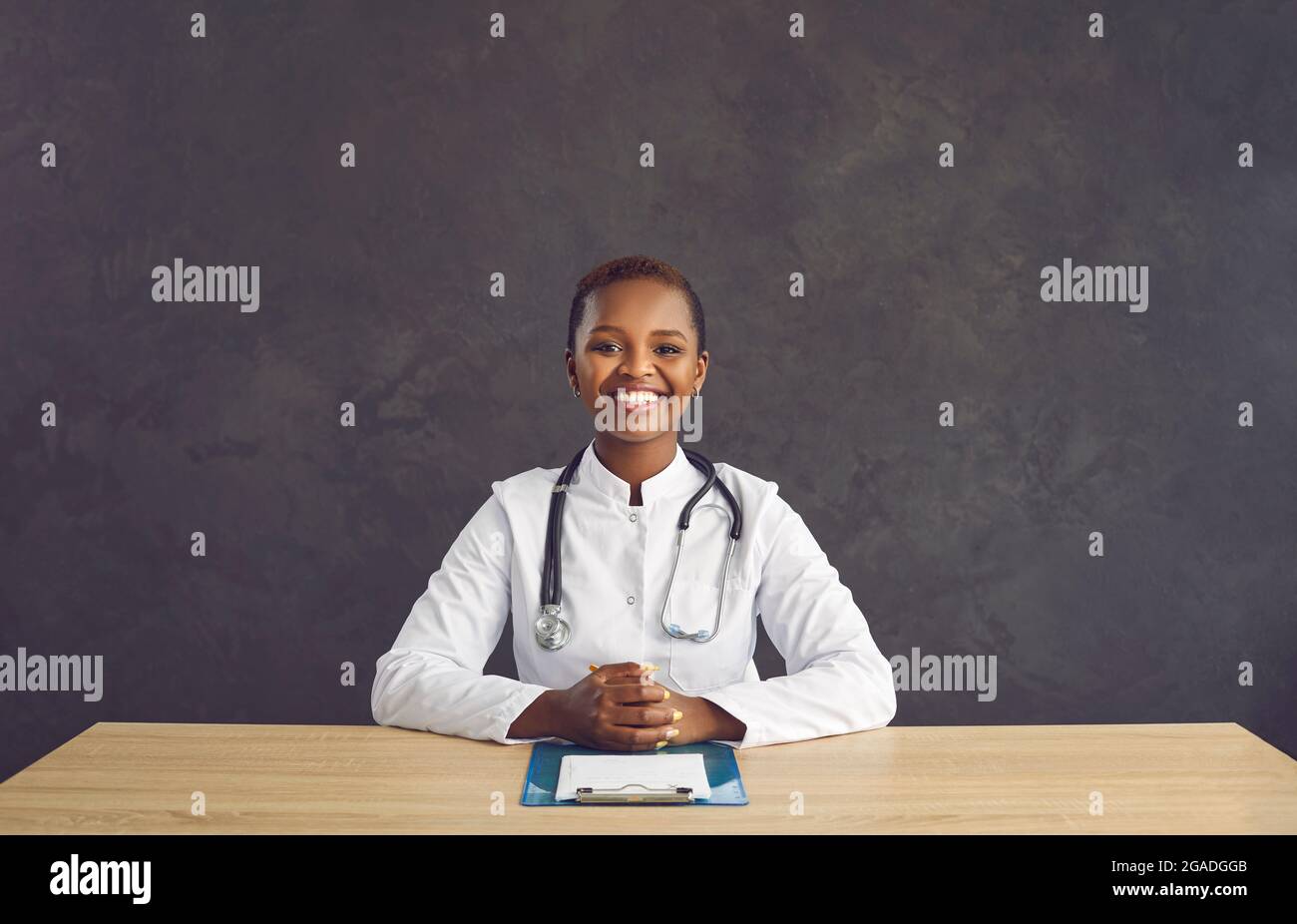 Portrait of happy black female doctor sitting at office desk and ...