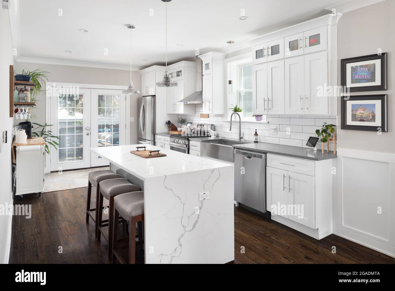 A white renovated kitchen with a waterfall granite island, stainless steel Whirlpool appliances, and hardwood floors. Stock Photo