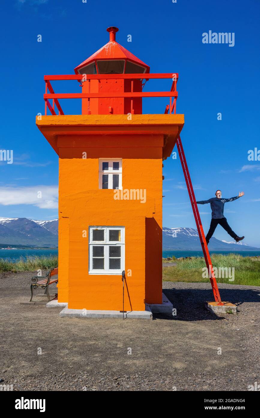 man hanging on the ladder of cute orange lighthouse svalbardseyri north iceland Stock Photo