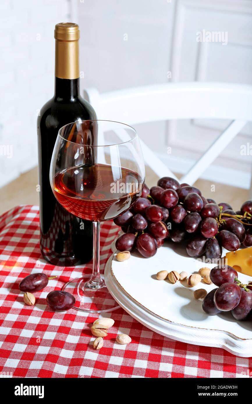 Red grape and cheese with glass bottle of wine on light interior