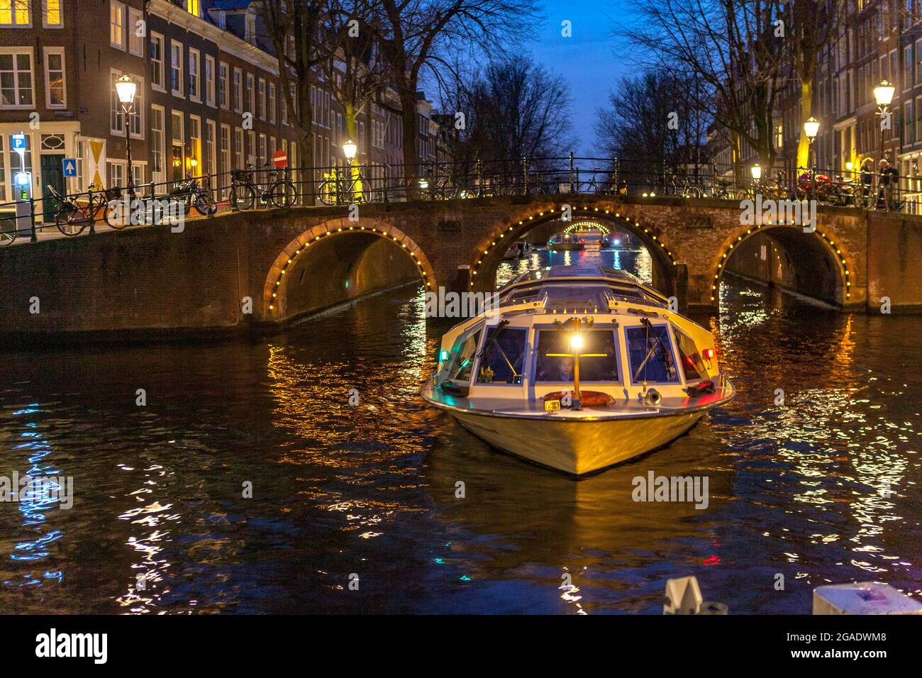 Tourist canal boat cruise and bridge with arches, illuminated at night, Herengracht and Leidsegracht canals, Amsterdam Stock Photo