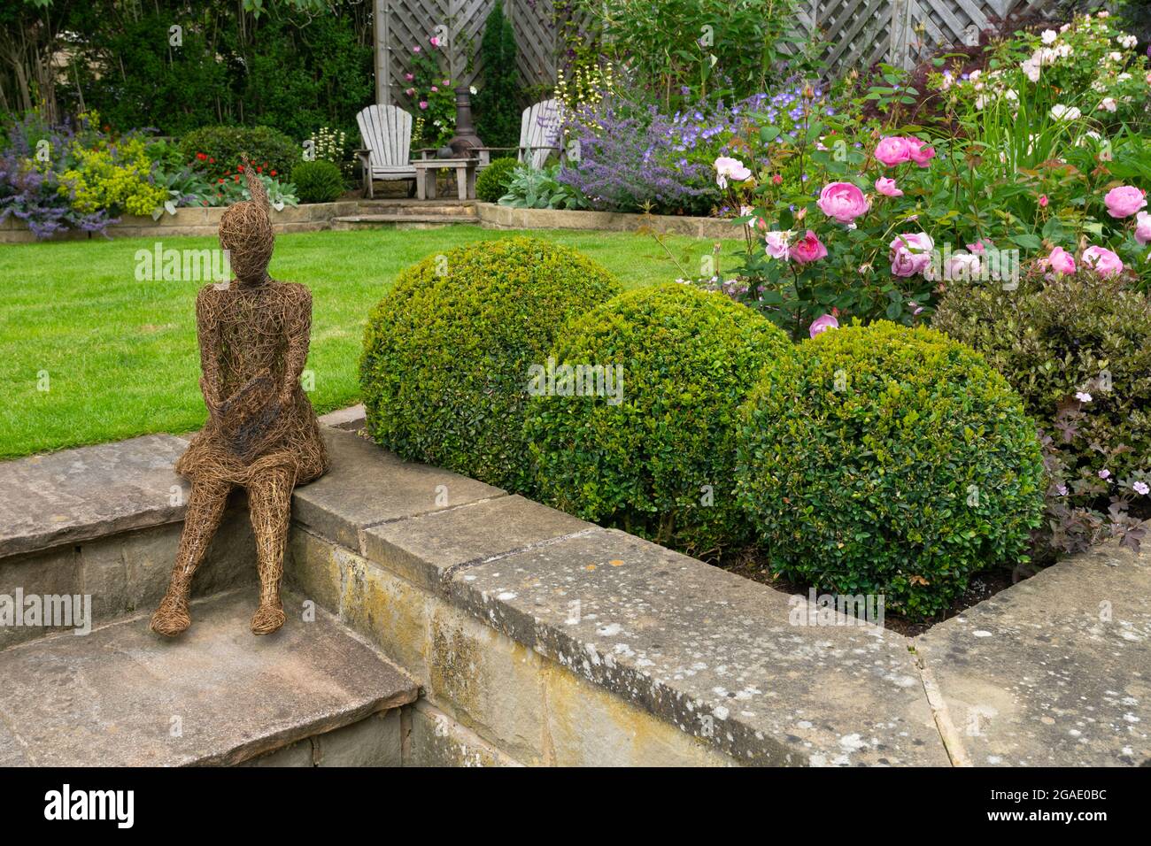 Sculpture art (ornamental feature) in beautiful colourful landscaped garden (flowering plants, shrubs, box balls, lawn, chairs) - Yorkshire England UK Stock Photo