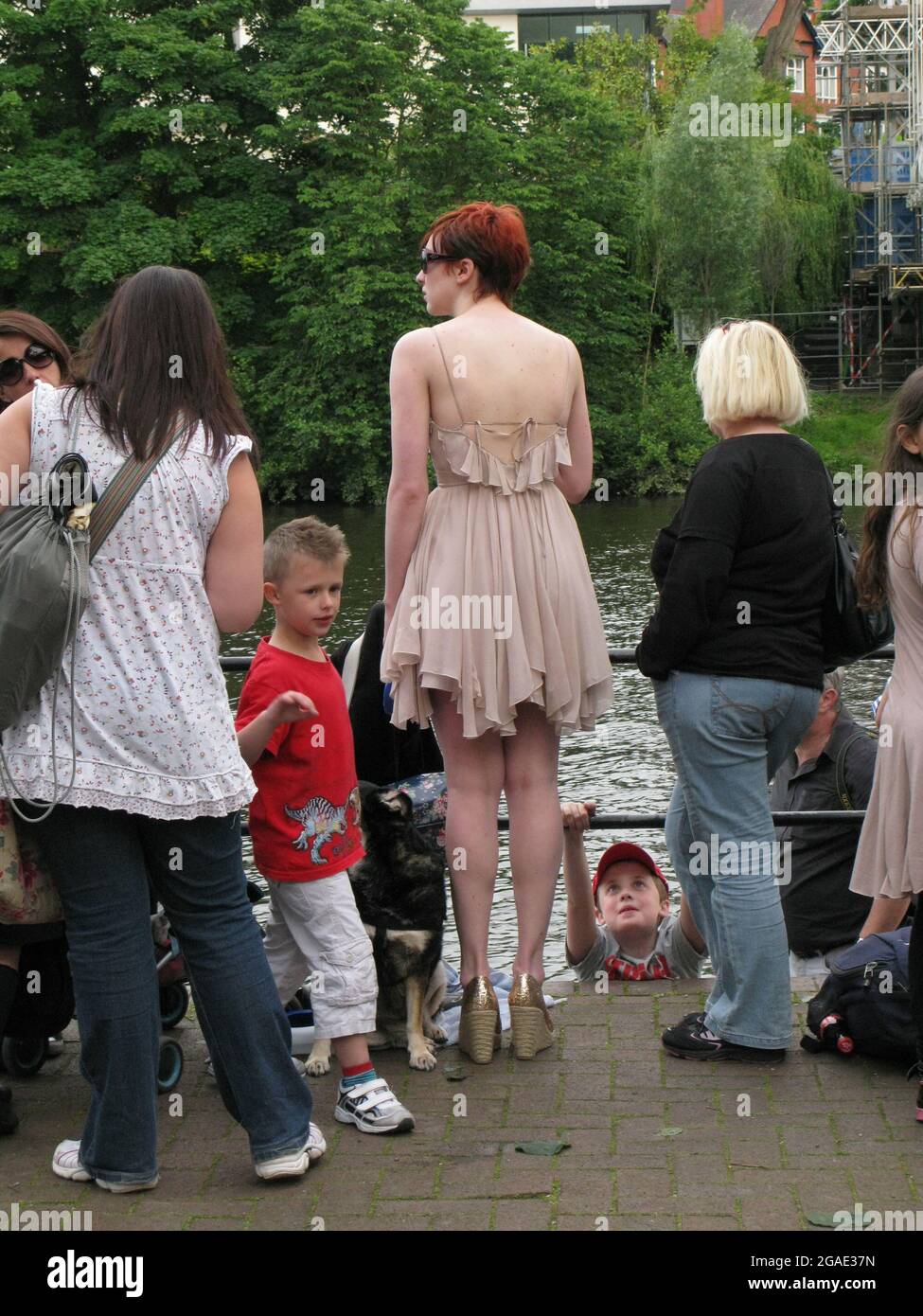A tall young red-headed woman on the riverside at Chester, Cheshire, England. She wears a stylish short dress and high heels. She has a dog on a lead Stock Photo